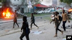 FILE - Security troops walk past burning cars after a fatal car bomb attack on a restaurant in Mogadishu, Somalia, May, 8, 2017. 