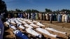 FILE - Men gather near bodies of people who were killed in a militant attack, during a mass burial at Zabarmari, in the Jere local government area of Borno state, in northeast Nigeria, Nov. 29, 2020.