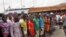 West Point residents stand behind a green string marking a holding area, as they wait for a second consignment of food from the Liberian Government to be handed out, at the West Point area, near the central city area of Monrovia, Liberia, Friday, Aug. 22,