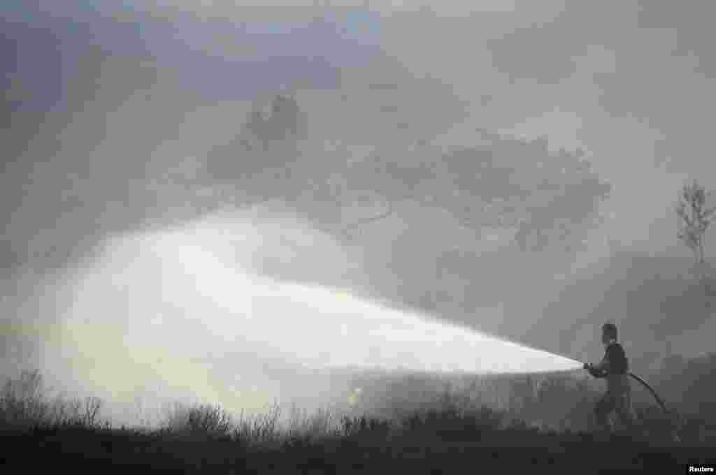 A firefighter hoses a brushfire on a moor above Carrwood, Britain.