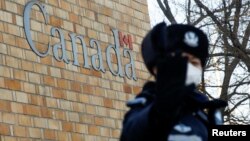 在加拿大驻北京大使馆外一名中国警察向摄影记者打手势。（2018年12月12日）