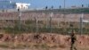 FILE - A Turkish soldier walks by the border fence with Syria while in the background, Kurdish fighters, top right, advance, as civilians, top left, flee the outskirts of Tal Abyad, Syria. 