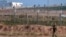 FILE - A Turkish soldier walks by the border fence with Syria while in the background, Kurdish fighters, top right, advance, as civilians, top left, flee the outskirts of Tal Abyad, Syria. 