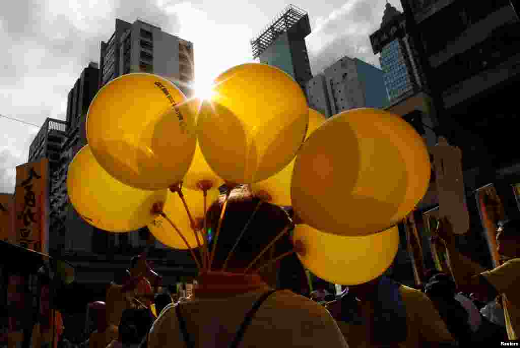 Seorang pengunjuk rasa membawa balon-balon berwarna kuning yang melambangkan payung-payung, sebuah simbol gerakan Occupy Central, selama pawai unjuk rasa pada hari peringatan ke-19 pengembalian kedaulatan Hong Kong ke penguasa China dari penguasa Inggris, di Hong Kong, China.