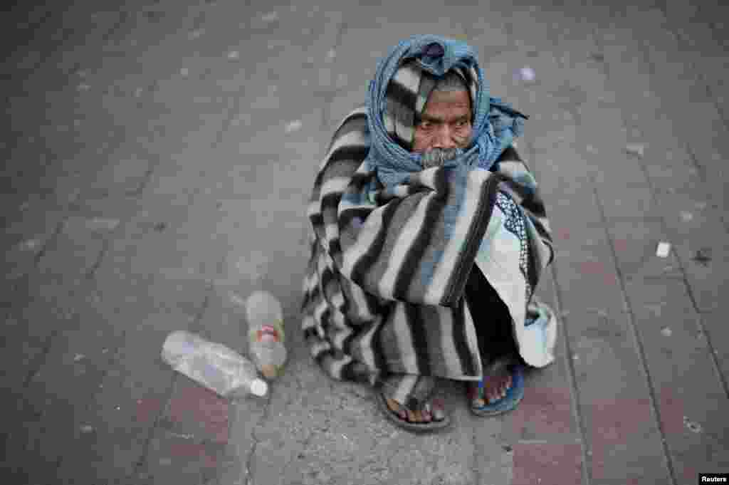 បុរស​ម្នាក់​ឃ្លុំ​ខ្លួនដោយ​ភួយ​នៅពេល​ដែល​លោក​អង្គុយ​នៅ​តាម​ផ្លូវ​ដើរ​ក្នុង​ព្រឹក​នៃ​រដូវ​រងារ​មួយ​ក្នុង​ទីក្រុង​ញូវដែលី​ប្រទេស​ឥណ្ឌា។