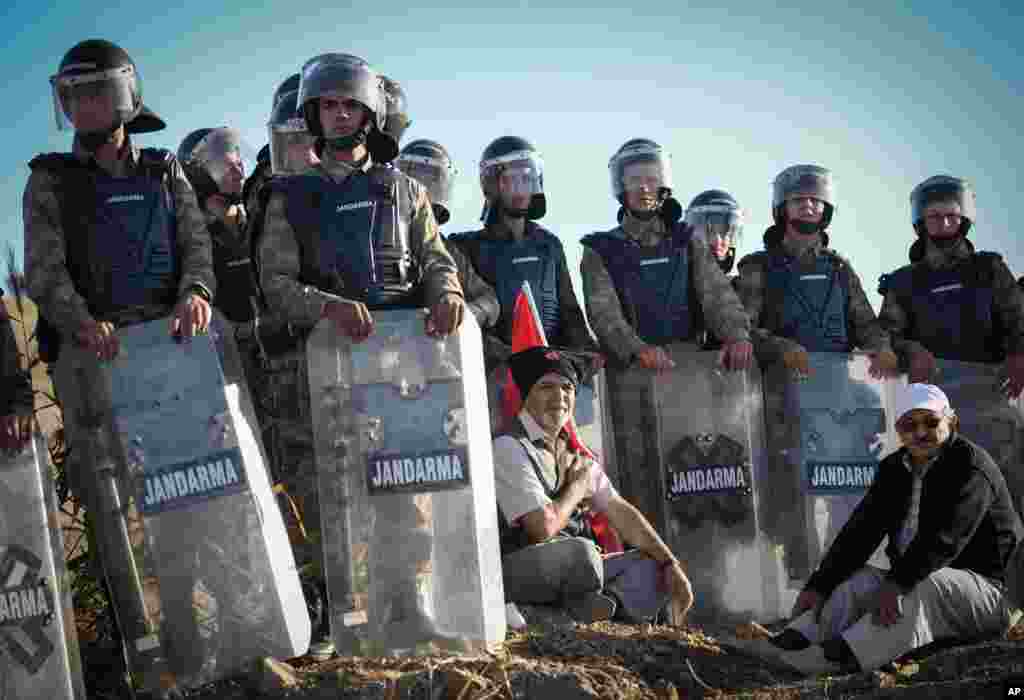 Seorang pria duduk sambil memegang bendera nasional Turki, sementara para petugas paramiliter memblokade ribuan warga yang berdemo di sekitar komples penjara Silivri di Turki. (AP Photo)