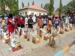 Widows and relatives of soldiers killed in battle stand behind food items they received from defense ministry authorities as part of a special remembrance event in Abuja, Nigeria, Jan. 11, 2020. (Timothy Obiezu/VOA)