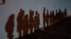 FILE - Asylum-seeking migrant families cast shadows on a wall as they form a queue to be processed by the U.S. Border Patrol after crossing the Rio Grande into the United States from Mexico in Roma, Texas, Aug. 12, 2021.