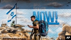 Израильский военный проходит мимо граффити с призывом вернуть заложников, похищенных во время нападения ХАМАС на Израиль 7 октября 2023 года. (AP Photo/Ariel Schalit)