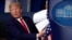 FILE - Then-President Donald Trump holds up papers in the James Brady Press Briefing Room of the White House on April 20, 2020, in Washington.