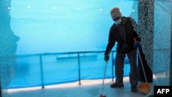 یک کارگر در حال جمع کردن شیشه های شکسته شده یک فروشگاه در حمله راکتی به اربیل در اقلیم کردستان عراق. ۱۶ فوریه ۲۰۲۱