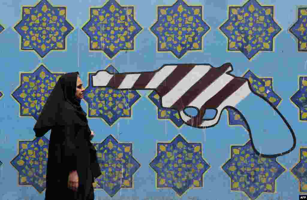 An Iranian woman walks past a mural depicting a gun painted on the wall of the former US embassy in the capital Tehran.