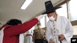 A South Korean Confucian scholar wearing a face mask to help protect against the spread of the new coronavirus has his temperature checked upon his arrival to cast his vote for the parliamentary elections at a polling station in Nonsan, South Korea,…
