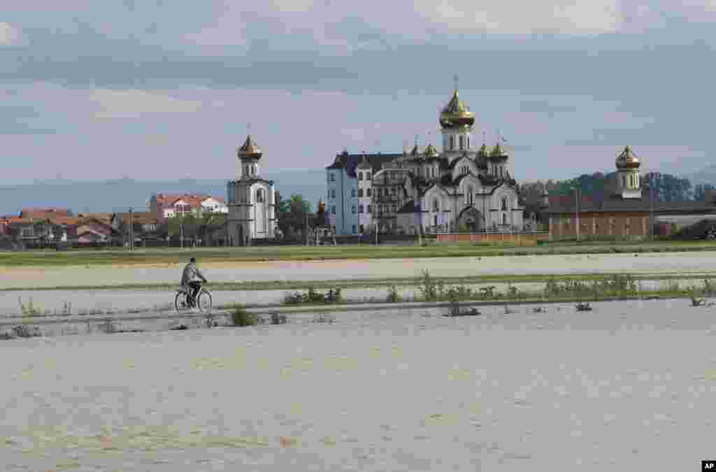 Seorang pria mengendarai sepeda menjauhi wilayah yang banjir di desa Dvorovi, dekat Bijeljina, Bosnia-Herzegovina (17/5). (AP/Amel Emric)