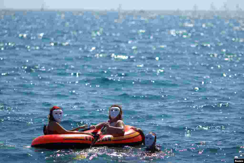 Tiga orang mencoba berlayar dengan perahu karet dari Eropa ke Afrika, sebagai simulasi perahu migran, dalam aksi unjuk rasa di pantai La Malagueta, Malaga, Spanyol selatan.