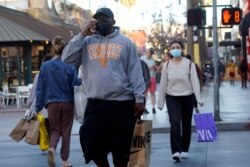 FILE - Shoppers wearing masks amid the COVID-19 pandemic cross a street on The Promenade in Santa Monica, California, June 9, 2021.
