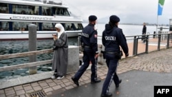 Police officers patrol as they pass by a woman wearing a traditional hijab headdress in Zell am See, Austria, Oct. 1, 2017. 