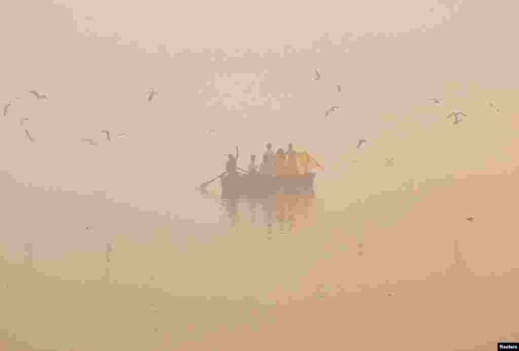 People take pictures on a boat on the Yamuna river on a smoggy morning in New Delhi, India.