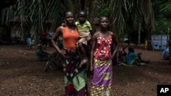 Monique Moukidje, 34, left, poses for a picture with her two children Marienne and Odalvia, in Mbangui-Ngoro, a Central African Republic village where she and hundreds of other displaced people who fled Bangassou found refuge, Feb. 15, 2021…