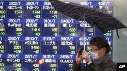 A man reacts to a gust of wind as it starts to snow, in front of an electronic stock board at a securities firm in Tokyo, Feb. 4, 2014.
