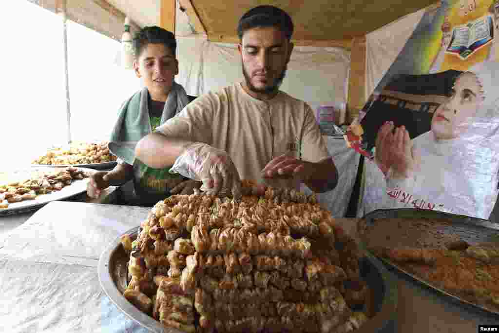 Seorang pengungsi Suriah menghidangkan kudapan untuk dijual selama Ramadan di kamp pengungsi Al Zaatri di Mafraq, Yordania, dekat perbatasan Suriah (30/7). (Reuters/Muhammad Hamed)