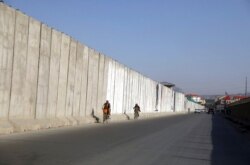 FILE - Afghan men ride their bicycles past blast walls protecting the Ministry of Interior Affairs, in Kabul, Afghanistan, July 3, 2021.