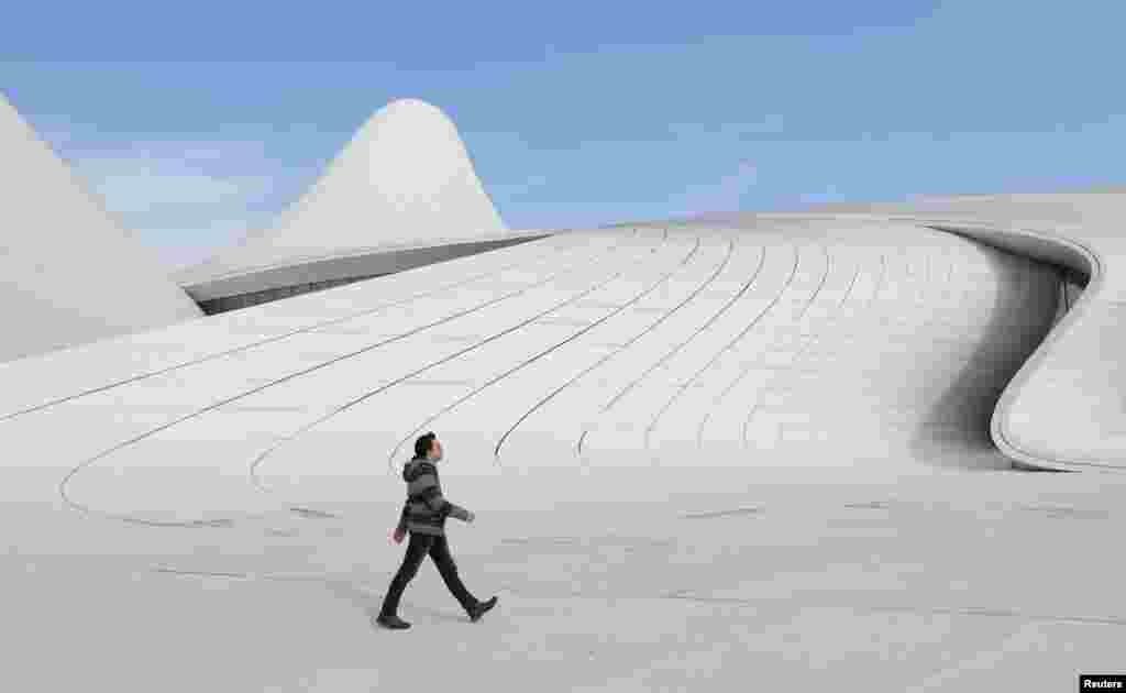 បុរស​ម្នាក់​ដើរ​នៅ​ខាងក្រៅ​មជ្ឈមណ្ឌល Heydar Aliyev ក្នុង​ទីក្រុង​ Baku ប្រទេស​អាស៊ែបៃហ្សង់។ &nbsp;