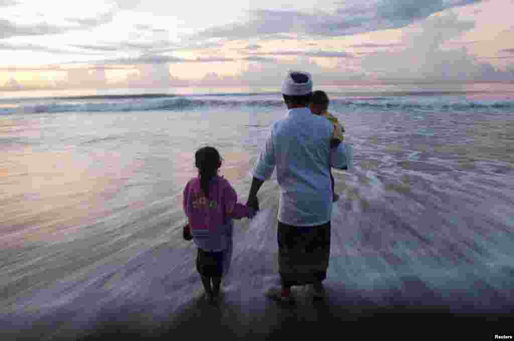 Sebuah keluarga Bali berdiri di pantai sambil menghadiri upacara sembayangan Melasti di pantai Gianyar, Bali. Melasti adalah upacara penyucian diri yang diadakan sehari sebelum Nyepi. Selama hari raya Nyepi, warga Hindu di Bali melakukan meditasi dan berpuasa, dan tidak boleh bekerja, memasak, menyalakan lampu, atau melakukan kegiatan apa pun.