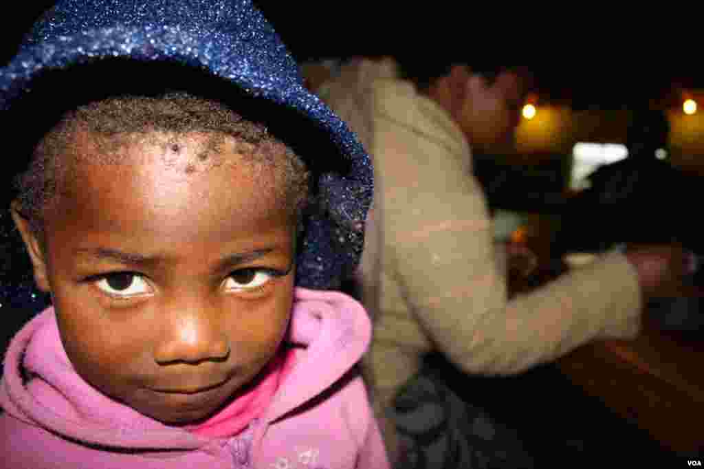 Lungiswa eats in the background, watched by her daughter, Lulama (VOA/ D. Taylor) 