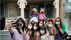 在香港迪士尼乐园，戴着口罩的游客与标志性卡通人物唐老鸭和黛丝鸭自拍。（2020年9月25日）