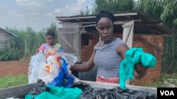 Aweko Faith, right, and Rachel Mema sort through polythene bags for washing, in Mpigi district, Uganda. (H. Athumani/VOA) 