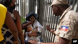 Seorang polisi Haiti meminta seorang wanita untuk menjauh dari gerbang Kedutaan Besar AS di Port-au-Prince, Haiti, Jumat, 9 Juli 2021. (Foto: AP)