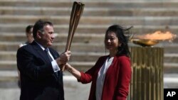 Hellenic Olympic Committee President Spyros Capralos, left, gives the Olympic torch to the former Japanese swimmer Imoto Naoko during the Olympic flame handover ceremony for the 2020 Tokyo Summer Olympics, in Athens, Thursday, March 19, 2020. 