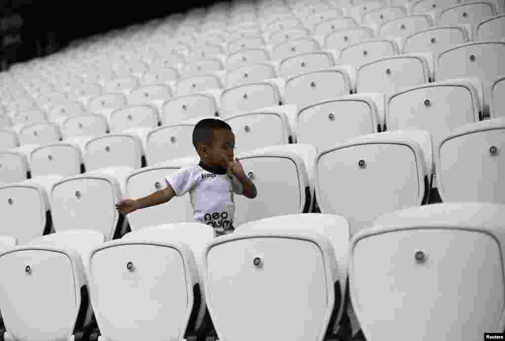 Seorang anggota keluarga dari seorang pekerja&nbsp; berjalan di antara jejeran bangku-bangku sebelum para pekerja bermain dalam sebuah pertandingan sepak bola untuk memperingati hari buruh di Arena Stadium Sao Paulo di Brasil, 1 April 2014. &nbsp;
