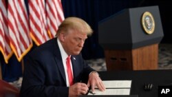 President Donald Trump signs one of four executive orders addressing the economic fallout from the COVID-19 pandemic at his Trump National Golf Club in Bedminster, N.J., Saturday, Aug. 8, 2020. Trump signed the executive orders and bypassed the…