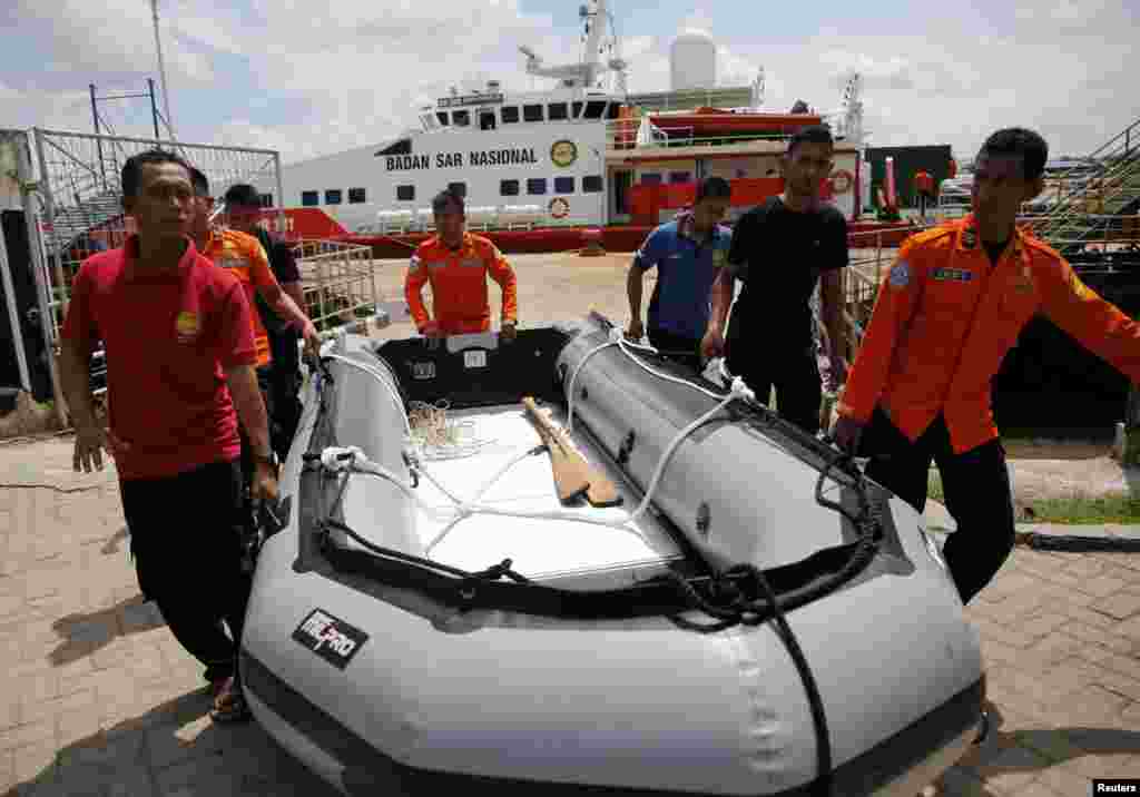 Para anggota tim penyelamatan membawa perahu karet di depan kapal SAR KN Purworejo dalam operasi pencarian untuk para penumpang AirAsia bernomor penerbangan 8501 di pelabuhan Kumai di Pangkalan Bun, Kalimantan Tengah (6/1). (Reuters/Beawiharta)