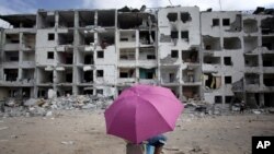 一名巴勒斯坦男孩打着伞在加沙地带北部的一处遭到破坏的居民区休息（2014年8月11日）