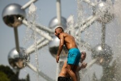Two men cool off in a public fountain near the Atomium during a summer hot day in Brussels, July 24, 2019.