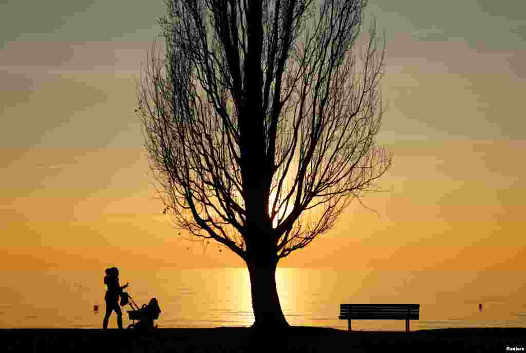 Seorang perempuan mendorong kereta bayi pada suatu senja di danau Leman di kota Lutry, Swiss.