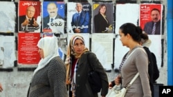 Perempuan-perempuan Tunisia melewati poster-poster kampanye pemilihan presiden di Tunis (21/11). (AP/Hassene Dridi)