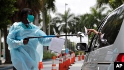 Healthcare worker Dante Hills, left, passes paperwork to a woman in a vehicle at a COVID-19 testing site outside of Marlins Park, July 27, 2020, in Miami.