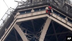 A rescue worker, top in red, hangs from the Eiffel Tower while a climber is seen below him between two iron columns Monday, May 20, 2019 in Paris. 