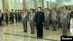 Pemimpin Korea Utara Kim Jong Un (tengah) berdiri memberi penghormatan di depan patung-patung mendiang pendahulunya di Istana Kumsusan di Pyongyang. 