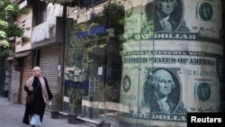 资料照：一位埃及女子走过开罗街头一处张贴着美元广告的外汇兑换处。（2024年5月9日）