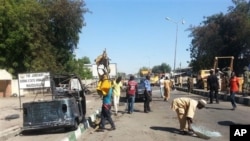 Petugas penyelamat membersihkan jalan menyusul bom mobil bunuh diri di sebuah pos militer di Maiduguri, Nigeria (14/1). (AP/Jossy Ola)
