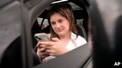 Alexis Bogan, whose speech was impaired by a brain tumor, uses an AI-powered smartphone app to create an audible drink order at a Starbucks drive-thru on Monday, April 29, 2024, in Lincoln, R.I. (AP Photo/Steven Senne)