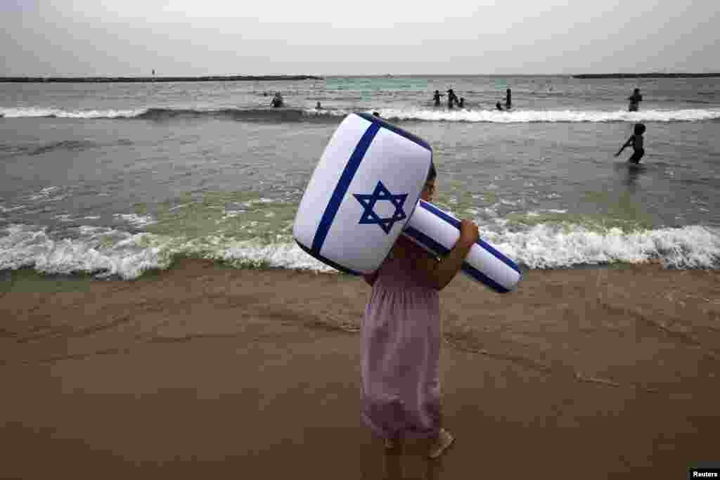 A girl holding to an inflatable hammer in the color of the Israeli flag stands on a beach at Tel Aviv during an aerial show as part of celebrations for Israel&#39;s Independence Day to mark the 66th anniversary of the creation of the state.