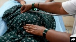 একজন সিনিয়র নার্স নয় মাসের গর্ভবতী মহিলাকে পরীক্ষা করার জন্য স্টেথোস্কোপ ব্যবহার করছেন। এপি ফাইল ছবি।