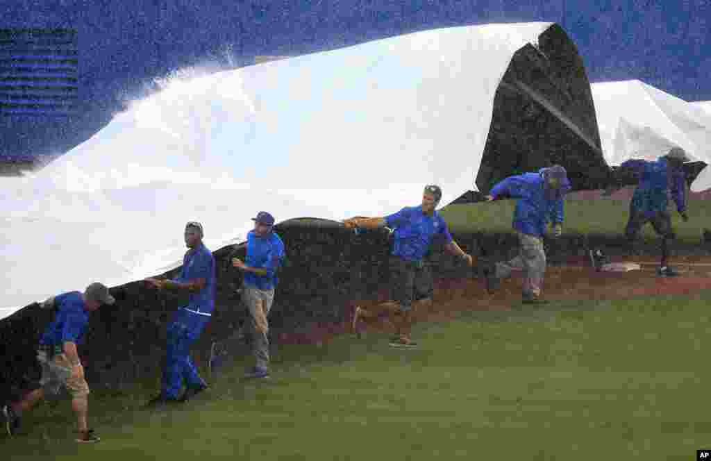 Members of the grounds crew pull a tarp across the field during a rain delay before the third inning of an NCAA college baseball game between Florida and Wake Forest in Gainesville, Florida, June 12, 2017.
