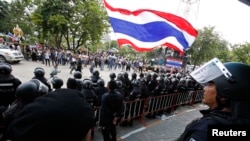 Demonstran anti-pemerintah melambai-lambaikan bendera nasional di depan polisi anti-huru-hara dan tentara yang menjaga stasiun televisi NBT di Bangkok (9/5). 
